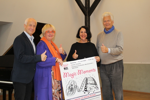 Zwei Männer und zwei Frauen stehen nebeneinander und halten das Plakat des Sommerlichen Musikfest 2025 in die Höhe.